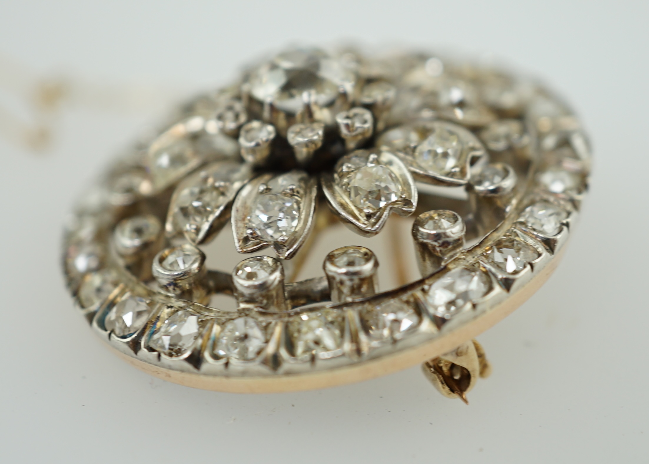 An Edwardian pierced gold and diamond cluster set circular brooch, with central cushion cut stone, diameter 34mm, gross weight 14.4 grams. Condition - fair to good